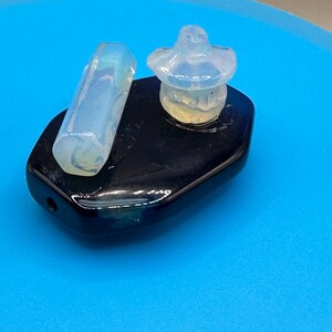 Puede incluir: Un objeto rectangular negro y brillante con un pequeño agujero en un extremo. Dos objetos translúcidos de color azul claro se encuentran encima: una forma cilíndrica y un tapón de botella. El fondo es una superficie azul brillante.