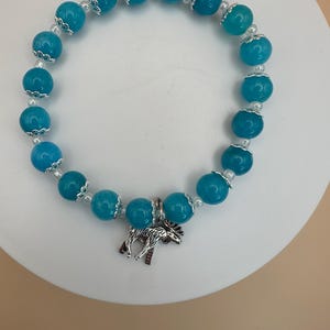 Könnte beinhalten: Ein türkisfarbenes Perlenarmband mit einem silbernen Elch-Anhänger. Die Perlen sind rund und haben einen silbernen Rand.