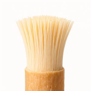 May include: A close-up shot of a brush with natural, pale yellow bristles and a light wood handle. The bristles are densely packed and splay outwards. This brush could be for applying paint, cosmetics, or cleaning.