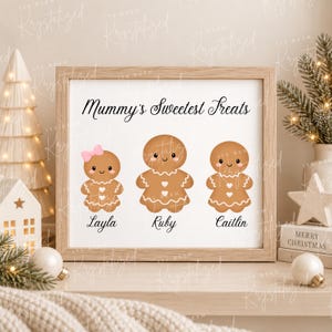 May include: A framed print featuring the text Mummy's Sweetest Treats above three gingerbread cookie illustrations. The first has a pink bow and the name Layla, the second is named Ruby, and the third is named Caitlin. Each cookie has white icing details.