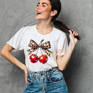 May include: White t-shirt with a graphic of two red cherries with a leopard print bow.