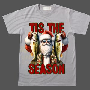 May include: A gray t-shirt with a white background and a red and green graphic of Santa Claus holding two fish. The text "Tis the Season" is printed in red and green on the shirt.