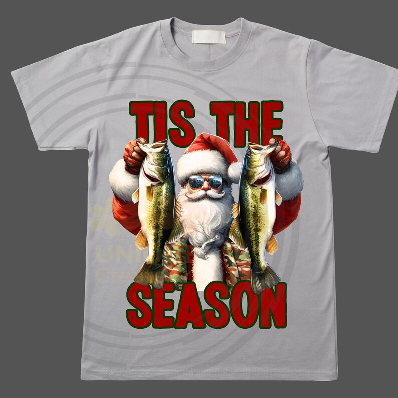 May include: A gray t-shirt with a white background and a red and green graphic of Santa Claus holding two fish. The text "Tis the Season" is printed in red and green on the shirt.