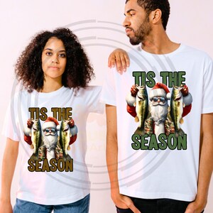 May include: White t-shirt with a graphic of Santa Claus holding two fish and the text "Tis the Season".
