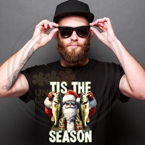 May include: A black t-shirt with a white graphic of Santa Claus holding two fish and the text "Tis the Season".
