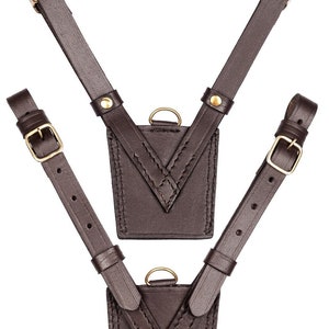 May include: Two brown leather chest harnesses with adjustable straps and gold-colored buckles. Each harness features a small, square pouch with a gold-colored ring and decorative stitching. The leather is a rich, dark brown color.