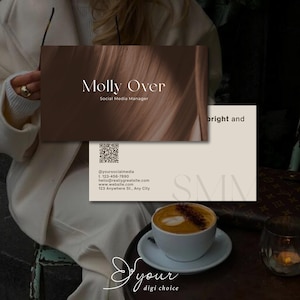 May include: Business cards with the text "Molly Over, Social Media Manager" in a minimalist design. The cards are brown and beige with contact information and a QR code. A cup of coffee sits on a saucer on a dark table.