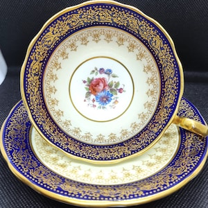 Vintage Aynsley dark blue and gold Teacup and saucer with floral pattern in the center.