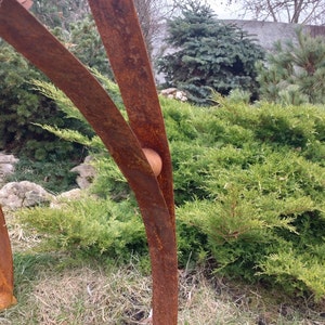 Pode incluir: Escultura abstrata de metal enferrujado. Apresenta elementos verticais curvos e um acento esf&eacute;rico, sobre um fundo de folhagem verde e c&eacute;u nublado. A obra de arte est&aacute; ao ar livre, provavelmente num jardim.