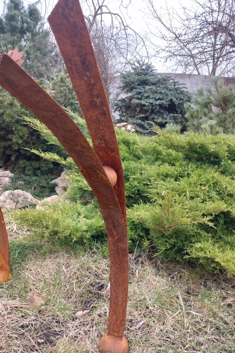 Pode incluir: Escultura abstrata de metal enferrujado. Apresenta elementos verticais curvos e um acento esf&eacute;rico, sobre um fundo de folhagem verde e c&eacute;u nublado. A obra de arte est&aacute; ao ar livre, provavelmente num jardim.