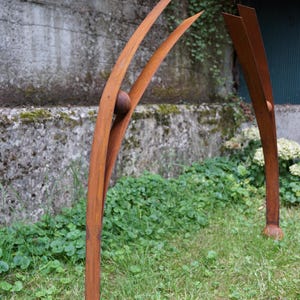 Pode incluir: Duas esculturas abstratas de metal com acabamento castanho-avermelhado desgastado. Uma apresenta dois elementos curvos e pontiagudos com uma esfera, a outra dois elementos retos e verticais. As esculturas est&atilde;o situadas numa &aacute;rea relvada, com um muro de bet&atilde;o ao fundo.