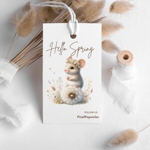 May include: A white tag with the text "Hello Spring" in brown lettering. A cartoon mouse with a flower crown sits on a dandelion. The text "Follow Us: PixelPopsicles" is at the bottom of the tag.