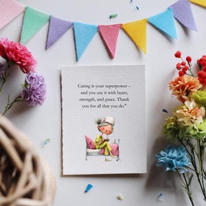 Puede incluir: Una tarjeta de felicitaci&oacute;n con el texto "Caring is your superpower - and you use it with heart, strength, and grace. Thank you for all that you do." La tarjeta presenta una ilustraci&oacute;n de una persona en la cama leyendo. Flores coloridas y una pancarta decoran el fondo.