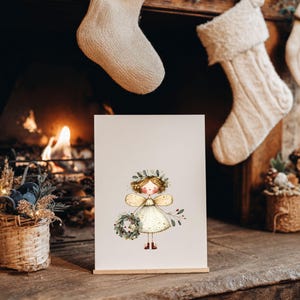 May include: A framed illustration of a fairy with a floral crown and wings, holding a wreath. The fairy is wearing a white dress with gold accents. The artwork is displayed on a wooden stand in front of a fireplace with Christmas stockings.