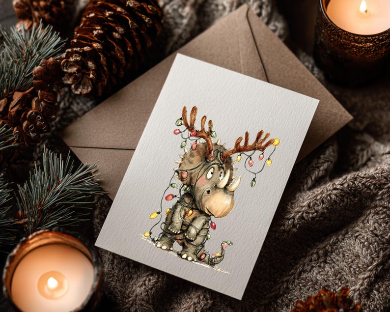 May include: A Christmas card featuring a whimsical illustration of a rhino adorned with antlers and wrapped in colorful Christmas lights. The rhino is wearing a jacket and has a small tail. The card is set against a cozy, textured background with pine cones and a lit candle.