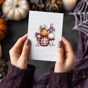 May include: A white rectangular card featuring a whimsical illustration of three stacked pumpkins with faces, including a central orange pumpkin, a bottom purple plaid pumpkin, and a white pumpkin on the right, all adorned with small decorative hats.