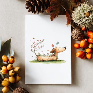 May include: A watercolour illustration of a dachshund dog lying on grass, decorated with flowers and butterflies. A small tree with pink blossoms grows from its back. The dog has a light brown coat and a blue collar. The artwork is on a white card.