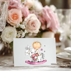 May include: A greeting card featuring a watercolor illustration of a child riding a rocking horse. The child is depicted with blonde hair and wearing a light-colored outfit. The rocking horse is white with a pink base, and a small stuffed animal is also on the horse.