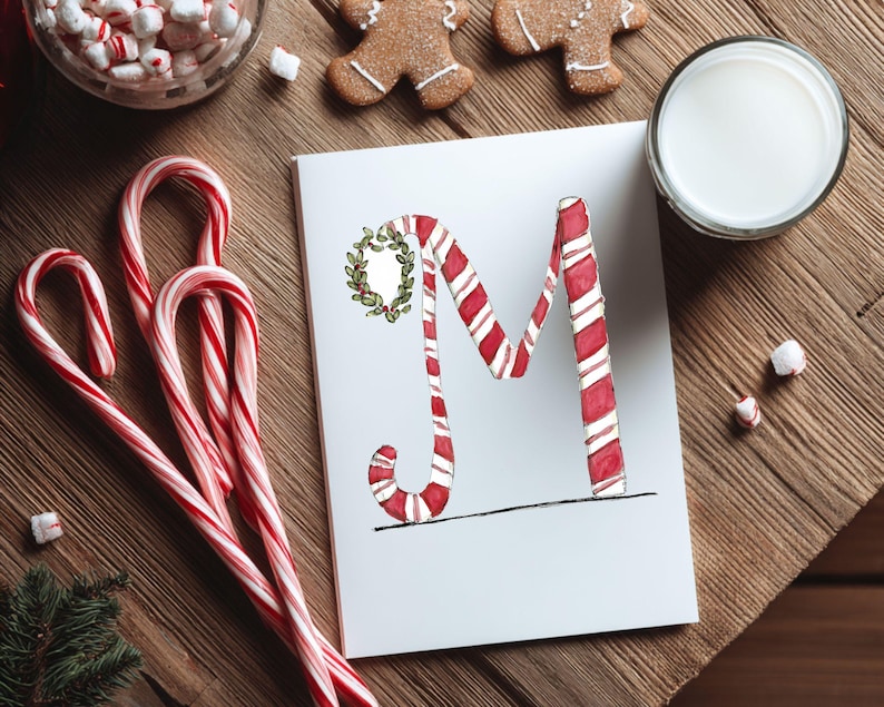 May include: A Christmas-themed image showing a white card with a candy cane-striped letter "M" decorated with a wreath. Candy canes, gingerbread biscuits, marshmallows, and a glass of milk are arranged on a wooden surface.