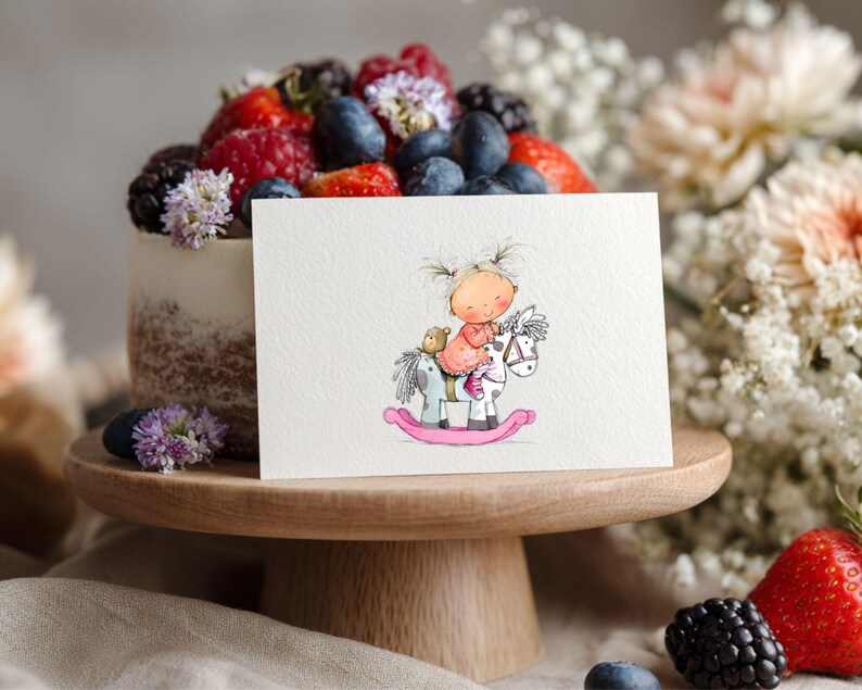 May include: A greeting card featuring a watercolor illustration of a child riding a rocking horse. The card is placed in front of a cake topped with berries and flowers, on a wooden cake stand. The scene is decorated with flowers and berries.
