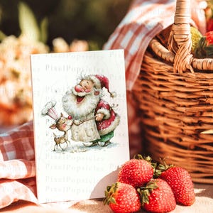 K&ouml;nnte beinhalten: Eine Gru&szlig;karte mit einer Aquarellillustration von Santa Claus und einem Rentier. Santa tr&auml;gt einen rot-wei&szlig;en Anzug und eine Kochm&uuml;tze. Die Karte befindet sich in der N&auml;he eines Picknickkorbs mit Erdbeeren. Der Text "Pixel Popsicles" ist sichtbar.