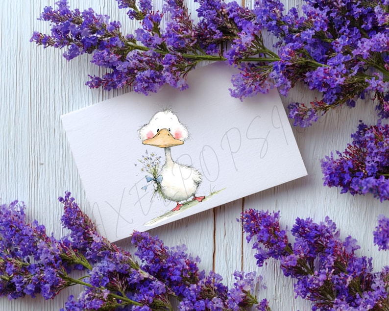 May include: A greeting card featuring a cartoon duck holding a bouquet of flowers, with a blue ribbon. The card is surrounded by purple flowers. The duck has a white body, a yellow beak, and pink cheeks. The background is a white wooden surface.