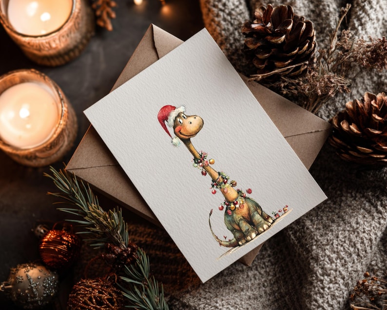 May include: A watercolor Christmas card featuring a friendly dinosaur wearing a Santa hat and festive garland. The card is on a neutral background with a brown envelope, pine cones, and candles, creating a cozy holiday scene.