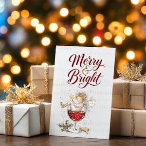 Peut inclure: Une carte de v&oelig;ux blanche avec le texte rouge Merry & Bright, illustrant un ange assis dans un verre &agrave; vin rempli de liquide rouge, entour&eacute; de bo&icirc;tes cadeaux emball&eacute;es dans du papier blanc et marron avec des rubans &agrave; paillettes dor&eacute;es.