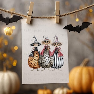 May include: A rectangular card suspended from a twine string by two wooden clips, displaying an illustration of three figures wearing witch hats. The figures are dressed in patterned outfits featuring leopard print, spots, and stripes, each holding a small doll.