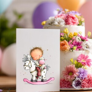 May include: A greeting card featuring a whimsical illustration of a child riding a rocking horse, holding a stuffed lamb. The card is set in front of a tiered cake decorated with colorful flowers and balloons, suggesting a birthday or celebration theme.