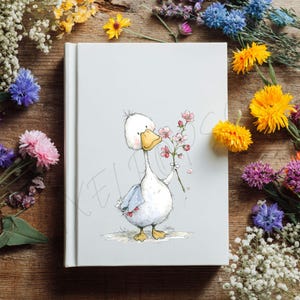 May include: A white journal with a whimsical illustration of a cartoon goose holding a sprig of pink flowers. The goose has a yellow beak and feet, and is wearing a blue scarf. The journal is surrounded by colorful flowers on a wooden surface.