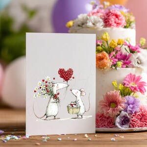 May include: A greeting card featuring two cartoon mice, one holding flowers and the other a basket. A red heart-shaped balloon floats above them. A two-tiered cake decorated with colorful flowers sits in the background.