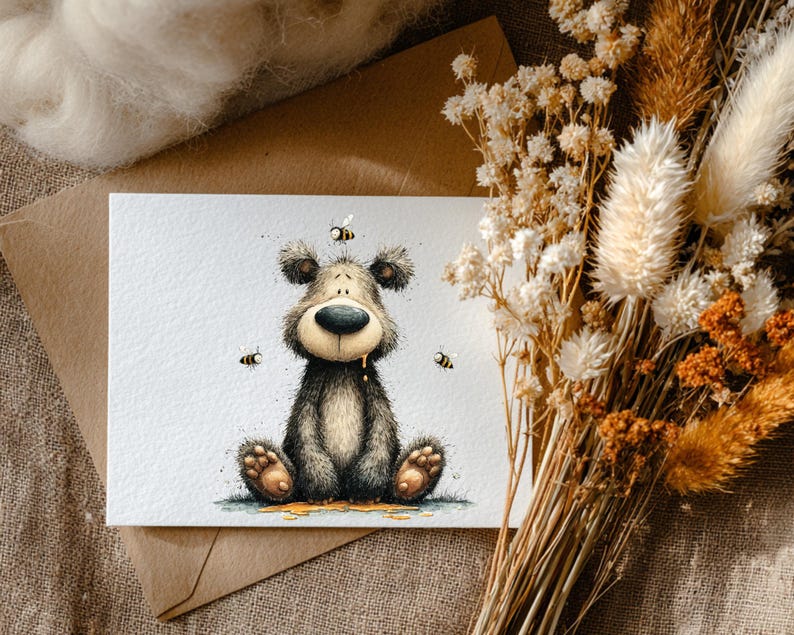 May include: A watercolour illustration of a bear with bees. The bear is sitting with honey dripping from its mouth. The image is on a white card with a brown envelope behind it. Dried flowers are in the background.