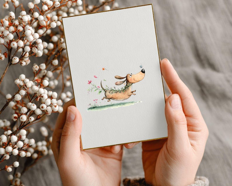May include: A greeting card featuring a cartoon dachshund dog running. The dog is depicted in brown and tan with a green garland. The card has a gold border and is held by a person. The illustration is set against a white background.