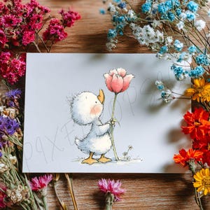 May include: A greeting card featuring a cartoon duckling holding a pink flower. The duckling is white with a yellow beak and feet, and a blush on its cheeks. The card is surrounded by dried flowers in various colors, including pink, blue, and yellow, on a wooden surface.