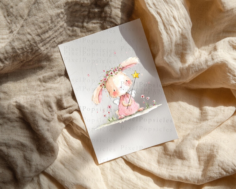 Op de afbeelding: Een rechthoekige print met een aquarelillustratie van een lichtroze konijn met een bloemenkrans op die een gele sterrenstaf vasthoudt. Het konijn heeft lange oren, kleine vleugels en staat op een ondergrond met kleine roze bloemetjes.