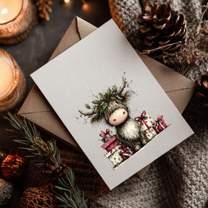 May include: A greeting card featuring a Highland cow illustration with a festive holly wreath and gifts. The card is on a brown envelope, with candles, pine cones, and ornaments in the background. A cozy, seasonal theme.