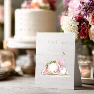 Op de afbeelding: Een witte wenskaart met een aquarelillustratie van een slapend wit konijntje met roze fee&euml;nvleugels en een bloemenkrans. Een kleine geel-zwarte bij vliegt boven het konijntje. De tekst PixelPopsicles is zichtbaar op de kaart.