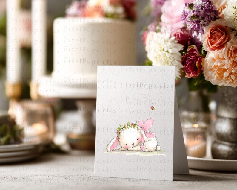 Op de afbeelding: Een witte wenskaart met een aquarelillustratie van een slapend wit konijntje met roze fee&euml;nvleugels en een bloemenkrans. Een kleine geel-zwarte bij vliegt boven het konijntje. De tekst PixelPopsicles is zichtbaar op de kaart.