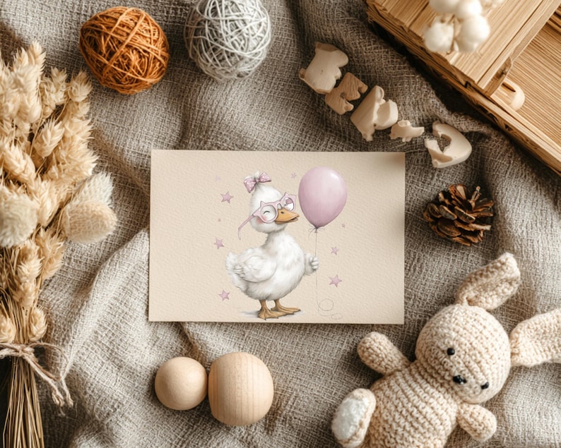 May include: A greeting card with a whimsical illustration of a white duck wearing glasses and a bow, holding a pink balloon. The card is surrounded by decorative items such as yarn balls, a wooden box, a pine cone, and a knitted bunny.