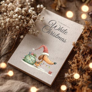 May include: A rectangular greeting card with a light beige textured surface featuring the text I'M DREAMING OF A White Christmas and an illustration of a brown dachshund wearing a red and white striped Santa hat, pulling a green sack.