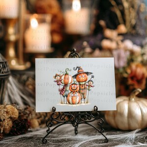 May include: A rectangular white card featuring a whimsical illustration of four stacked and standing pumpkins with faces, wearing hats and scarves, displayed on a black metal easel stand. The pumpkins are orange, white, and striped.
