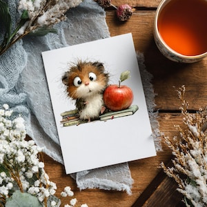 May include: A greeting card featuring a whimsical illustration of a fluffy, brown and white creature with large eyes, perched on a stack of books next to a red apple. The card is on a blue cloth with white flowers and a cup of tea.