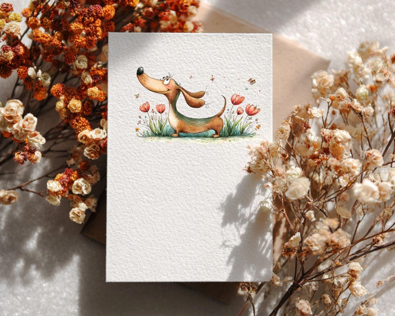 May include: A blank greeting card with a watercolour illustration of a dachshund dog. The dog has brown fur and a green belly, and is in a field of grass and flowers. The card is surrounded by dried flowers.