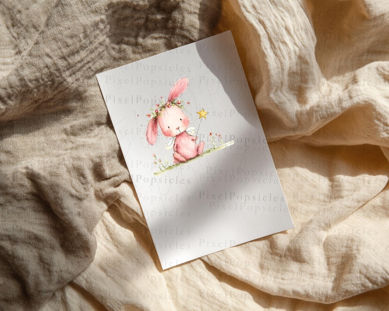 Op de afbeelding: Een rechthoekige witte kaart met een aquarelillustratie van een roze konijn met een bloemenkrans en kleine witte vleugels. Het konijn houdt een gele sterrenstaf vast en zit op een dunne groene lijn. De tekst PixelPopsicles is zichtbaar.