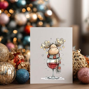 Peut inclure: Une carte de v&oelig;ux pr&eacute;sentant une illustration de dessin anim&eacute; d'un &eacute;lan portant une &eacute;charpe ray&eacute;e rouge et blanche, avec des guirlandes lumineuses autour de ses bois, debout dans un grand verre &agrave; vin rempli de vin rouge, entour&eacute; de flocons.
