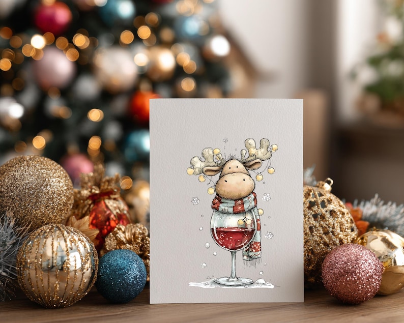 Peut inclure: Une carte de v&oelig;ux pr&eacute;sentant une illustration de dessin anim&eacute; d'un &eacute;lan portant une &eacute;charpe ray&eacute;e rouge et blanche, avec des guirlandes lumineuses autour de ses bois, debout dans un grand verre &agrave; vin rempli de vin rouge, entour&eacute; de flocons.