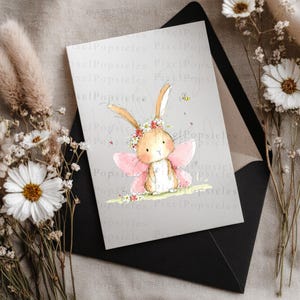 Op de afbeelding: Een rechthoekige wenskaart met een aquarelillustratie van een lichtbruin konijntje met roze fee&euml;nvleugels en een bloemenkrans. Het konijntje staat op een stukje gras met een kleine bij en kleine rode hartjes in de buurt.