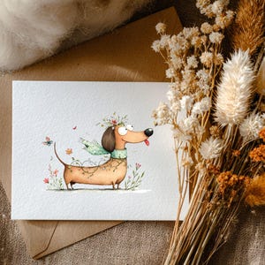May include: A watercolour illustration of a dachshund dog adorned with a floral crown, scarf, and garland. The dog has a long body, short legs, and a joyful expression. Butterflies and flowers surround the dog on a white card.