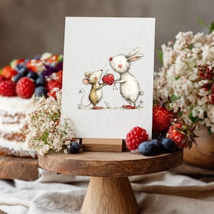 May include: A greeting card featuring a whimsical illustration of a mouse and a rabbit holding a heart. The card is displayed on a wooden stand, with a cake and berries in the background. The image has a soft, watercolor style.